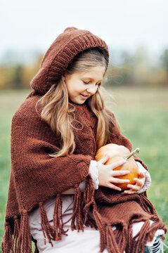 Happy little girl on pumpkin patch on cold autumn day, with a lot of pumpkins for Halloween or thanksgiving.