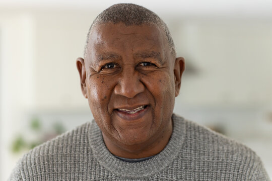 Senior African American man making eye contact smiling in kitchen with potted plant gray sweater
