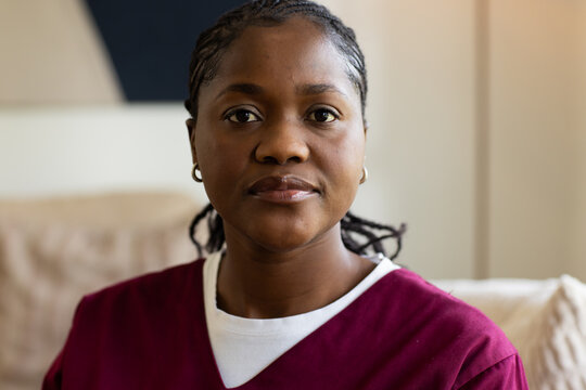 Mid adult African woman sitting on light couch wearing maroon top, hoop earrings, beige cushion