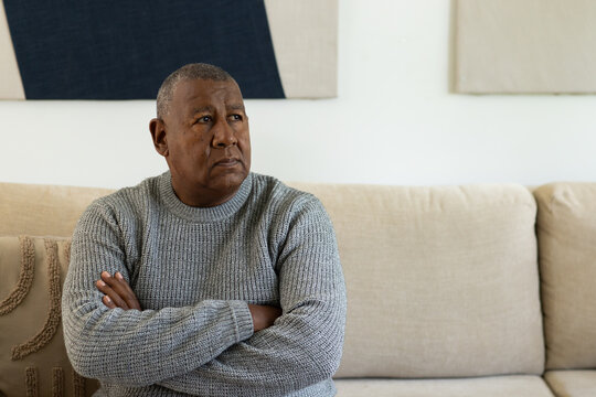 Senior African American man sitting on beige sofa in living room, wearing gray sweater