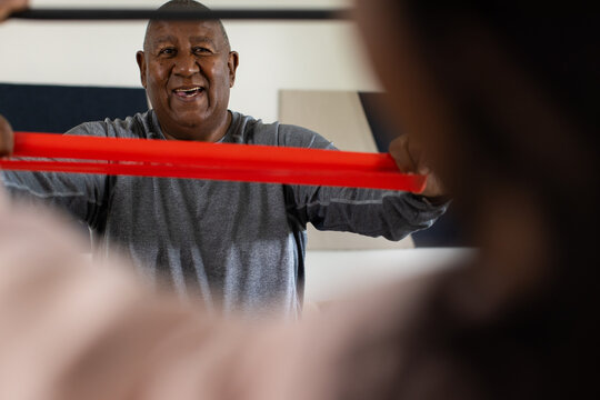 Senior African American man holding red resistance band, stretching at home in grey shirt