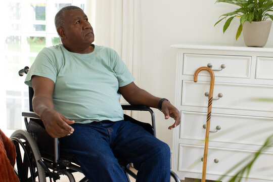Senior African American man sitting in wheelchair at home, wearing green T-shirt and holding cane