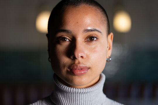 African American adult woman facing camera, wearing ribbed turtleneck and hoop earrings in cafe