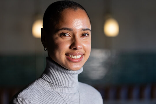 African American woman smiling directly at camera in cafe near pendant lamps and teal tiled wall
