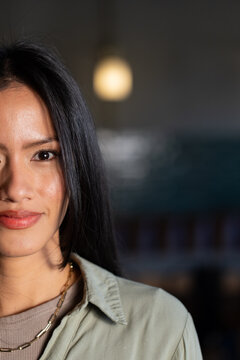 Mid-adult Asian woman posing, wearing sage green shirt and gold necklace in cafe, copy space