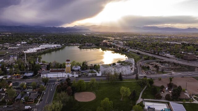 Aerial view of the historic wooden roller coaster at Lakeside Amusement Park beside a lake with surrounding urban landscape under a cloudy sky in Denver, Colorado, United States.