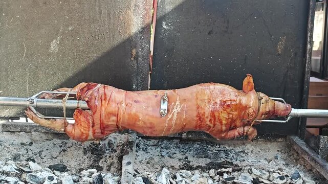 A whole piglet slowly roasting on a spit over hot coals, with golden crispy skin and traditional open-fire cooking.
