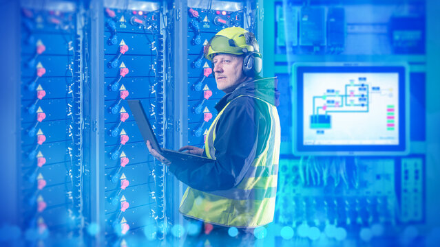 Energy storage facility, engineer uses a laptop to inspect and configure industrial battery systems for electricity storage, power distribution and grid management.