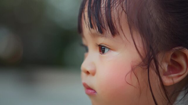 Close up side profile of cute Asian toddler girl looking into distance with curious expression, detailed child eye and face portrait outdoors, childhood curiosity, observation