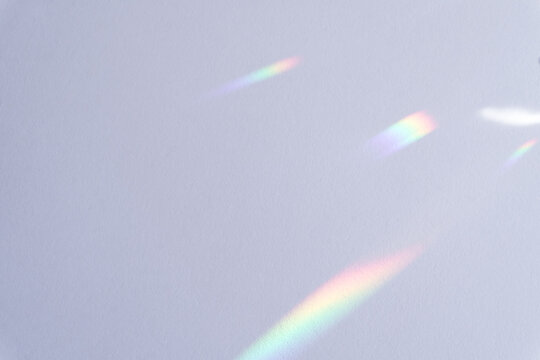 Horizontal photo of soft prism light refractions and colorful rainbow flares on a clean white wall surface with copy space.