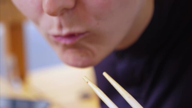 Woman enjoys sushi with chopsticks, dipping avocado wrapped rolls into soy sauce before eating. Close up food moment shows focused, satisfied tasting of colorful vegetarian rolls at table.