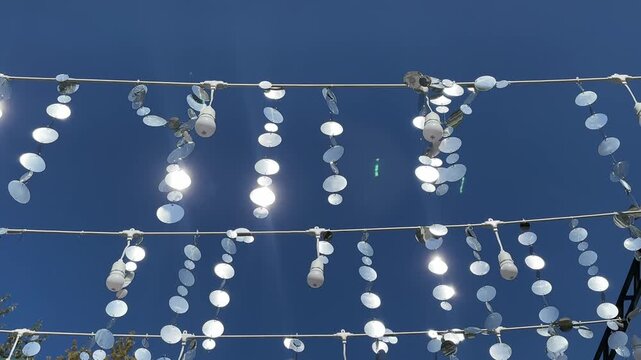 Hanging mirror sequins and light bulb garlands sparkling in sunlight against clear blue sky for outdoor party decor concept