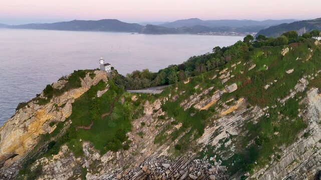 Aerial view of Getariako Itsasargia lighthouse perched on a rocky cliff overlooking the sea during golden hour in Getaria, Euskadi, Spain.