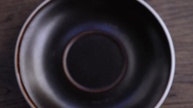 Hands slide coffee cup to inspect latte art. White foam leaf pattern remains clear as cup settles on saucer, reflecting precise cafe drink presentation and focused attention as hand adjusts drinkware.