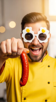 Man in yellow chef coat and egg-shaped glasses holds a sausage, concept of fun food, humor, and culinary delight, with free space