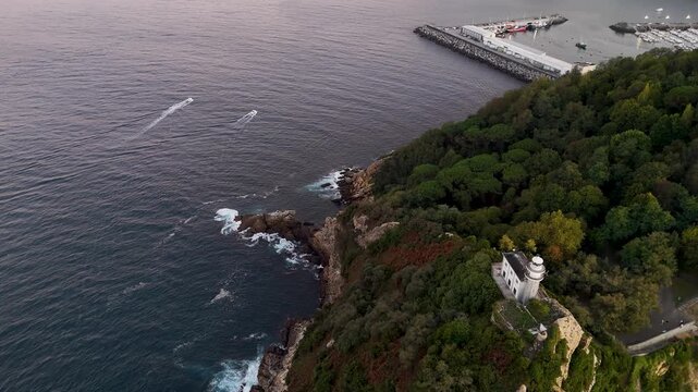 Aerial view of Getaria Lighthouse perched on a cliff overlooking the sea with boats in the water in Getaria, Euskadi, Spain.
