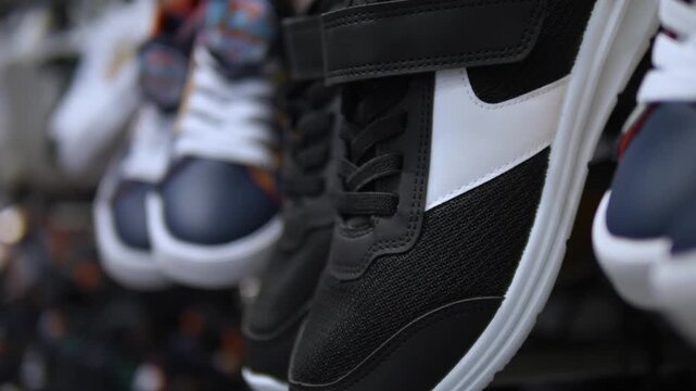 Black sneakers with white panels dangle in shop display, gently moving among other shoes. Hanging footwear fills frame, highlighting sporty design, laces, and textured soles in shallow focus.