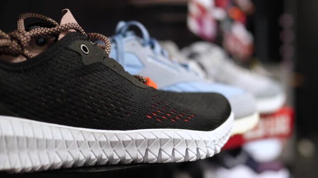 Retail sneaker display features black shoe in sharp focus beside pale blue pairs. Store shelf presentation highlights textured outsole and lace details, creating clean commercial mood.