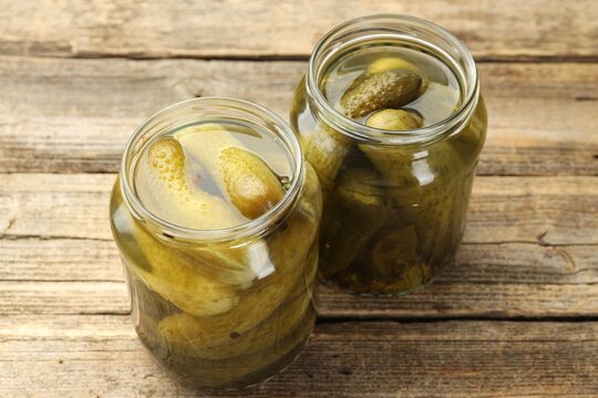 Pickled cucumbers in glass jars on wooden table, closeup