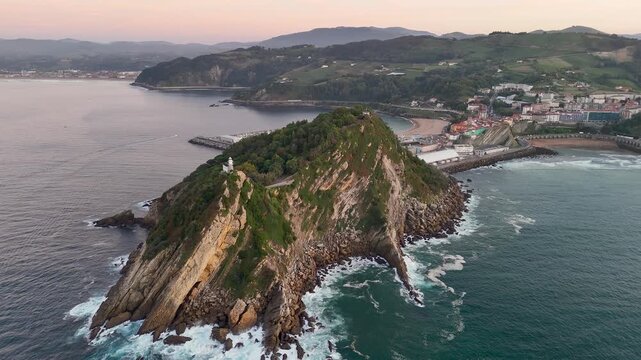 Aerial view of Getariako Itsasargia lighthouse on the rocky San Anton peninsula with the town of Getaria in the background at sunset in Getaria, Euskadi, Spain.