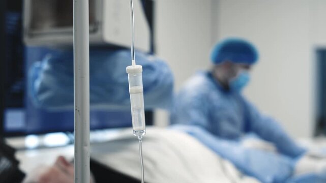 IV drip and intravenous infusion in the foreground during a medical procedure in a hospital angiography room.