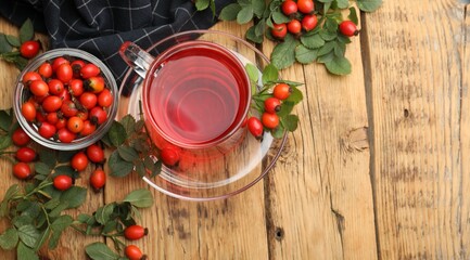 Hot rosehip tea and berries with leaves on wooden table, flat lay. Space for text © New Africa