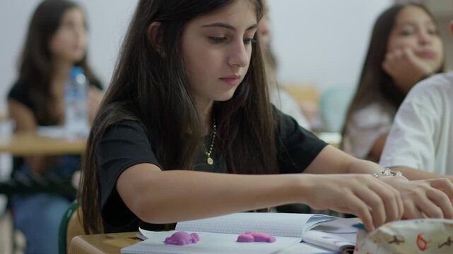 Focused student writing in a notebook during a classroom lesson with peers in the background