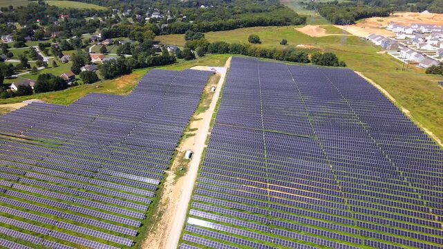 Camera drifts left across solar arrays with houses beyond the installation in 4K video.
