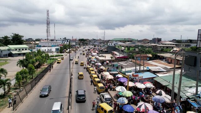 Aerial view of the busy Ojodu Berger street with yellow buses, street vendors, and pedestrians in Ojodu Berger, Lagos, Nigeria.