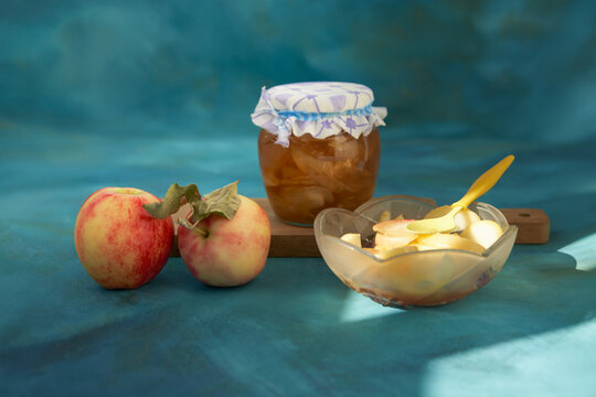 Making jam from Streifling apples. Two apples and apple jam in a jar and a small bowl, set against a blue background with faint strokes of gold leaf.