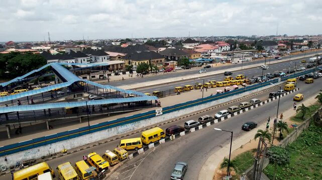 Aerial view of the busy Ojodu Berger bus terminal with yellow danfo buses parked along the highway and pedestrians crossing the footbridge in Ojodu Berger, Lagos, Nigeria.