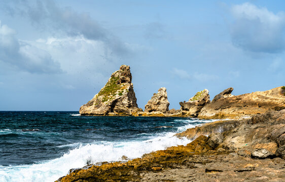 Dramatic view of the rocky coast and limestone sea stacks at Pointe des Chateaux, Guadeloupe, surrounded by crashing ocean waves under a blue sky.