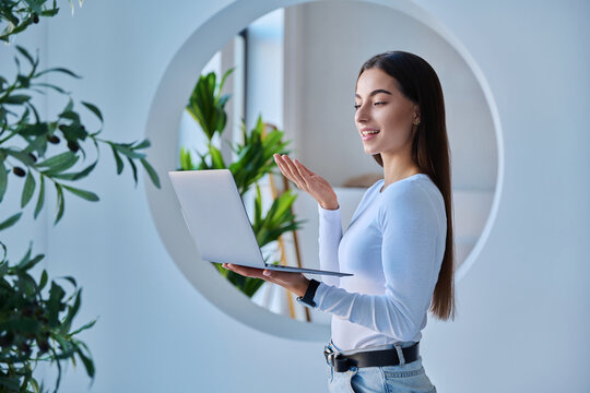 Young female student video calling or presenting on laptop in modern campus setting