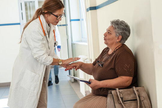A female doctor talks with a patient who is waiting in the hospital hallway for their appointment. The conversation feels calm and friendly as they discuss the upcoming examination.