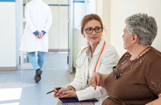 A female doctor talks with a patient who is waiting in the hospital hallway for their appointment. The conversation feels calm and friendly as they discuss the upcoming examination.