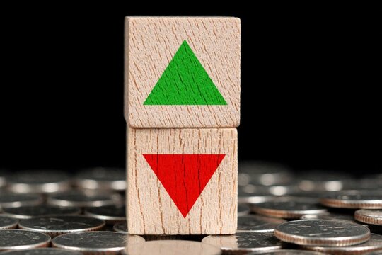 Two wooden blocks with green up arrow, red down arrow stand on pile of coins. Business concept of financial growth loss. Stock market trend shows profit, deficit in economy. Success, failure symbol