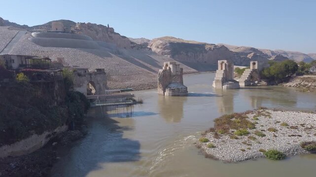 Hasankeyf Old Bridge ruins in Turkey, medieval stone piers standing in the Tigris River beside a gravel embankment, before the Ilisu Dam flooding