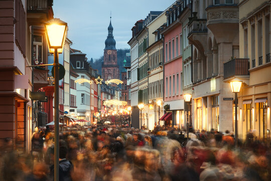 Loads of people with motion blur rushing and shopping on the historic German city of Heidelberg at Christmas. With holiday decoration and buildings leading to a church.