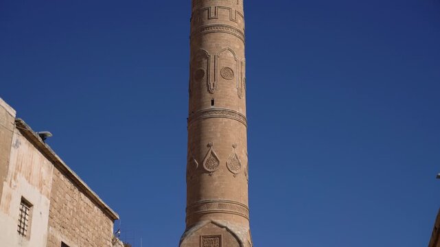 Ulu Cami minaret with carved stone medallions and a square kufic panel, Great Mosque of Mardin, Turkey, rising above old stone walls