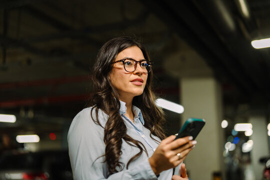 Woman holding smartphone looking away in parking garage