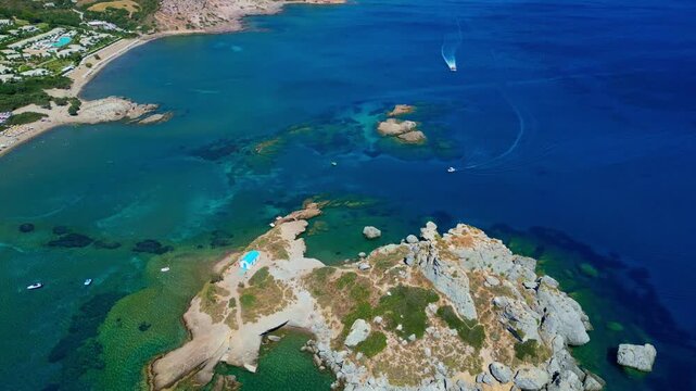 An aerial drone shot showcasing the picturesque rocky islet of Kastri located in Kefalos Bay, opposite Agios Stefanos Beach on Kos Island, Greece. The vibrant turquoise and azure waters of the Aegean 