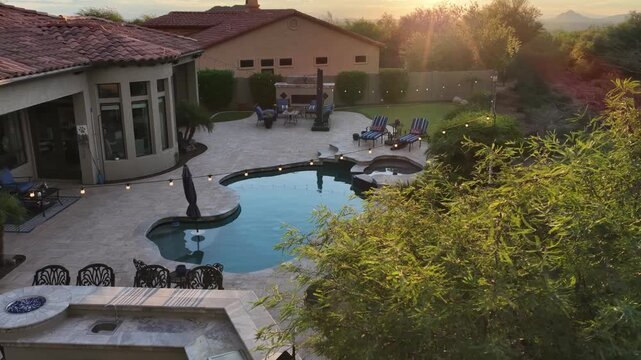 A 4k video of a desert landscaped backyard in Arizona featuring a travertine tiled pool deck, outdoor kitchen , spa and fireplace.