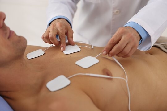 Doctor attaching ECG electrodes to patient's chest in clinic, closeup