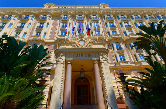 Facade of the historic Carlton Hotel with flags, ornate balconies and Rolex clock on the Croisette, Cannes, French Riviera, France