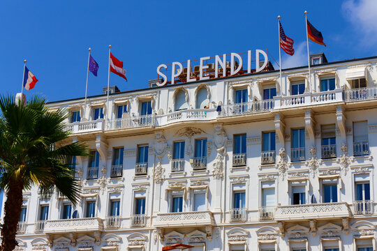 Ornate white facade of the Splendid Hotel with international flags and rooftop sign against blue sky, Cannes, French Riviera, France