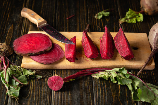Sliced beetroot rests beside kitchen knife on wooden cutting board, with peeled wedges and greens nearby. Vibrant beet displays rich color and natural texture for healthy cooking inspiration.