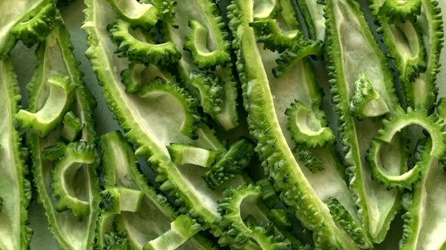 Preparation of exotic raw bitter melon for cooking. Tightly arranged bitter gourd halves with the white core removed, topped with small, sliced half-moons.