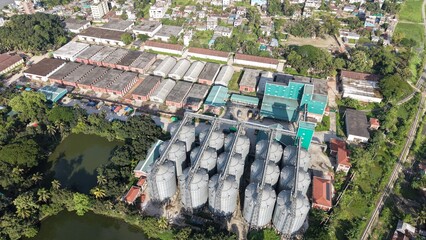 Aerial view of a large grain storage facility with multiple steel silos and warehouses near a residential area © ridwanhassan