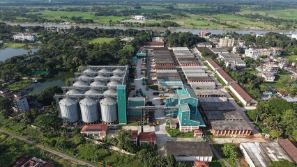 Aerial view of a large industrial grain storage facility with metal silos and warehouses located near a river in a rural landscape © ridwanhassan