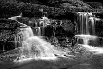 Atmospheric black and white long exposure of small cascades flowing over layered rocks in Monbach Valley, Black Forest, Germany. © ON-Photography